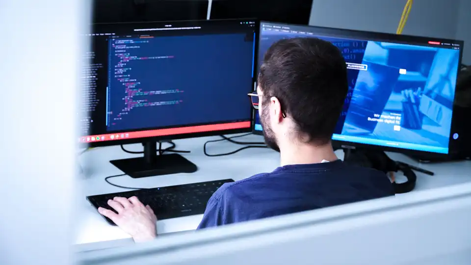 Webentwickler in Drupal-Agentur sitzt an einem Schreibtisch und schaut auf Monitor