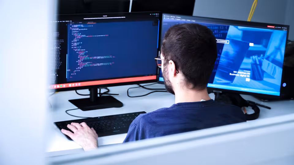 Eine Person sitzt an einem Schreibtisch und schaut auf den Monitor