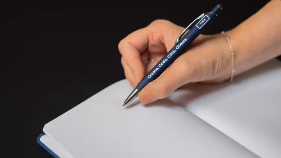 Eine Hand, die etwas mit einem Kugelschreiber in einen Block schreibt