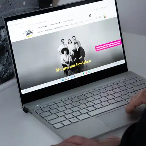 Eine Person sitzt vor einem aufgeklappten Laptop, auf dem die Karriereseite der Justiz NRW aufgerufen ist.