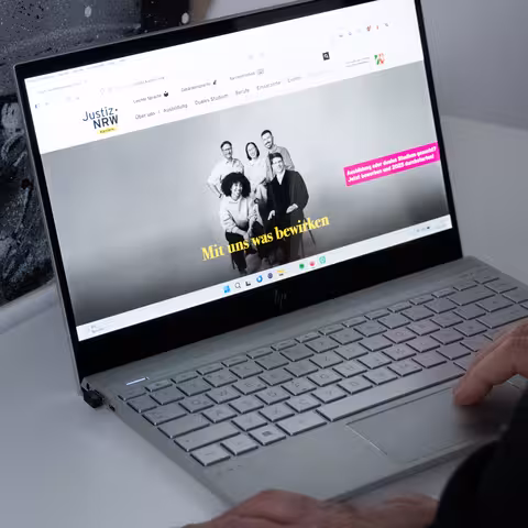 Eine Person sitzt vor einem aufgeklappten Laptop, auf dem die Karriereseite der Justiz NRW aufgerufen ist.