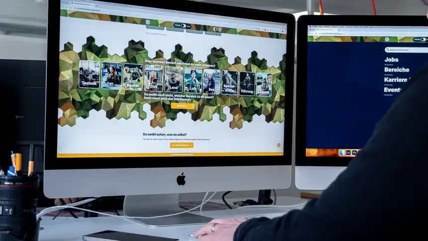 Zwei Apple Monitore, die die Karriereseite der Bundeswehr zeigen, davor eine Person, die auf den Bildschirm schaut.