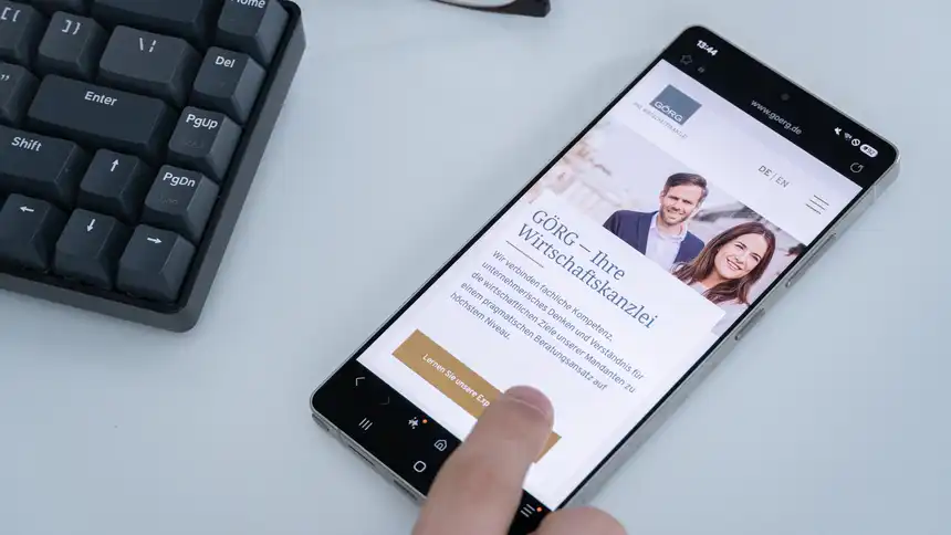 Ein Mobilgerät liegt auf dem Tisch. Ein Finger tippt auf einen Link der aufgerufene GÖRG-Website