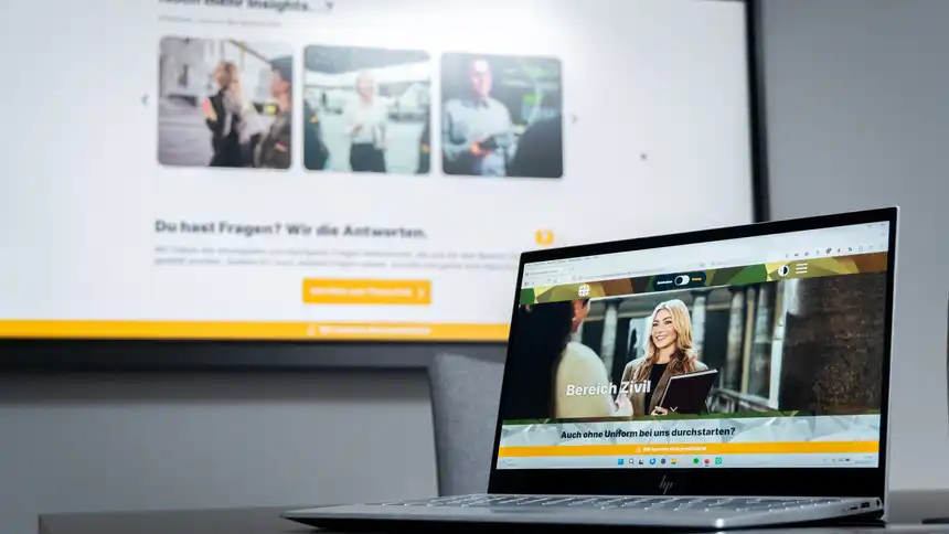 Ein Display an der Wand, auf dem die Karriereseite der Bundeswehr zu sehen ist. Davor ein Laptop, das ebenfalls die Karriereseite zeigt.