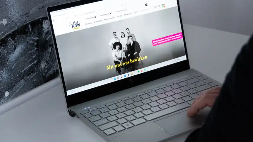 Eine Person sitzt vor einem aufgeklappten Laptop, auf dem die Karriereseite der Justiz NRW aufgerufen ist.