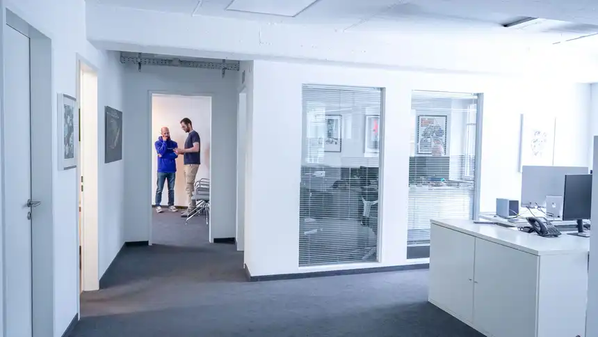 Blick in ein offenes Büro, im Hintergrund stehen zwei Personen