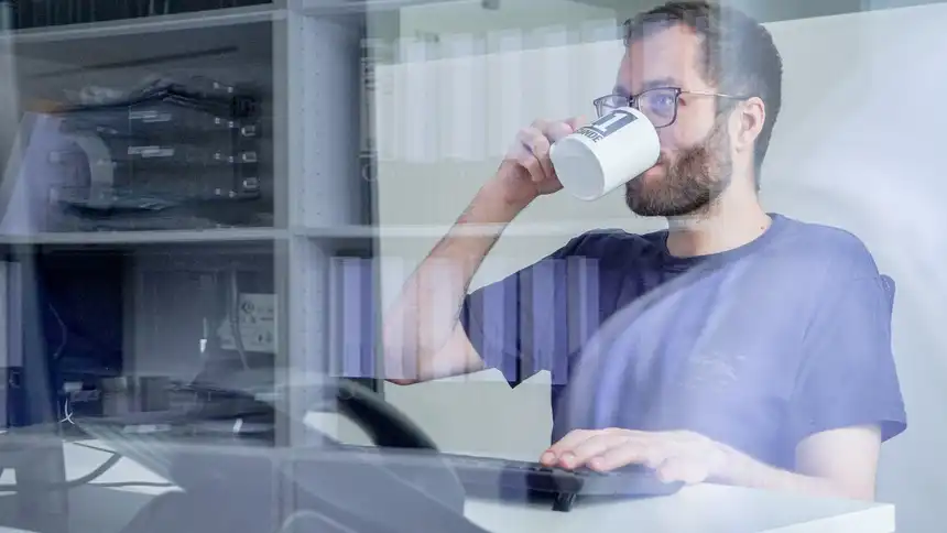 Eine Person sitzt an einem Schreibtisch und trinkt aus einer Tasse