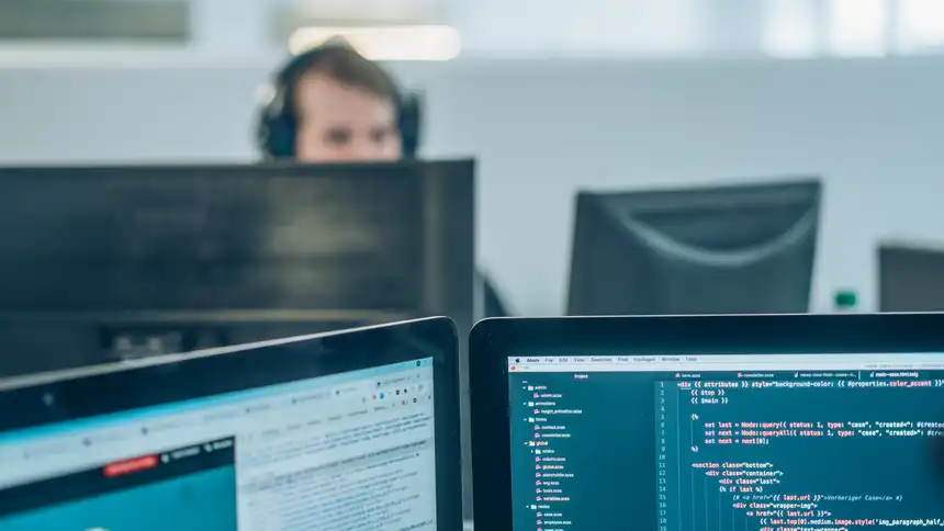 Mehrere Computerbildschirme, im Hintergrund eine Person