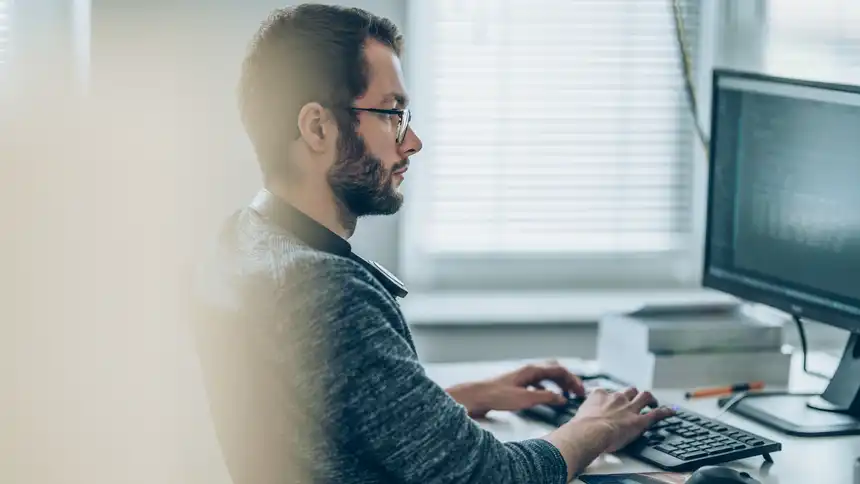 Eine Person sitzt an einem Schreibtisch und tippt auf einer Computertastatur