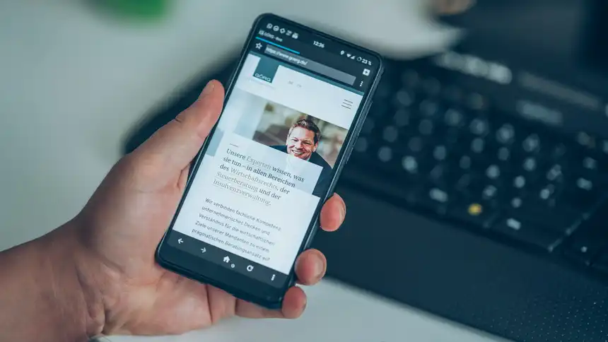 Eine Person am Schreibtisch hält ein Mobilgerät in der Hand