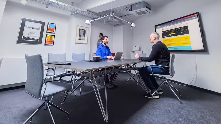 Zwei Personen sitzen in einem Besprechungsraum an einem großen Konferenztisch