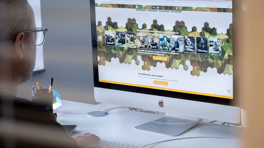 Ein Apple Monitor, der die Karriereseite der Bundeswehr zeigt, davor eine Person, die auf den Bildschirm schaut.