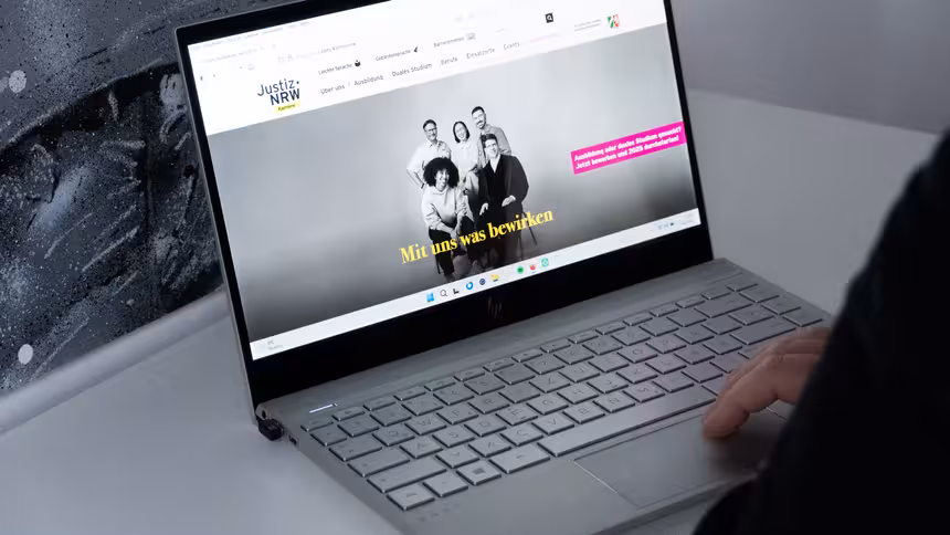 Eine Person sitzt vor einem aufgeklappten Laptop, auf dem die Karriereseite der Justiz NRW aufgerufen ist.