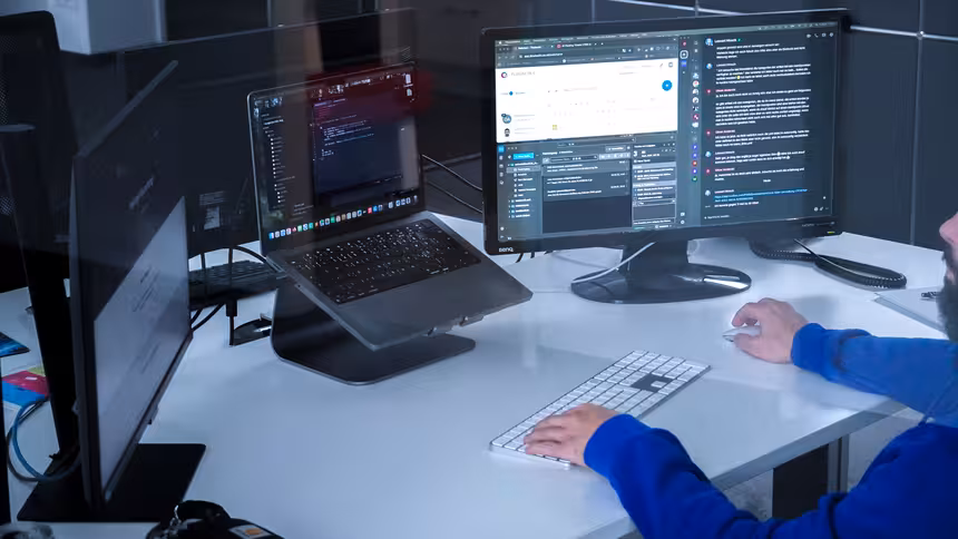 Eine Person sitzt an einem Schreibtisch und schaut auf einen Monitor