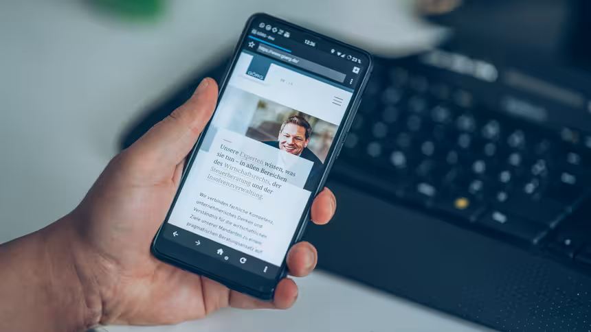 Eine Person am Schreibtisch hält ein Mobilgerät in der Hand