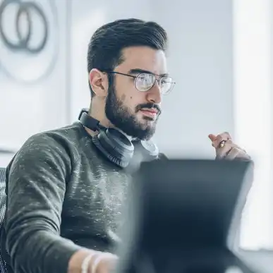 Eine Person mit Kopfhörern um den Hals schaut auf einen Monitor